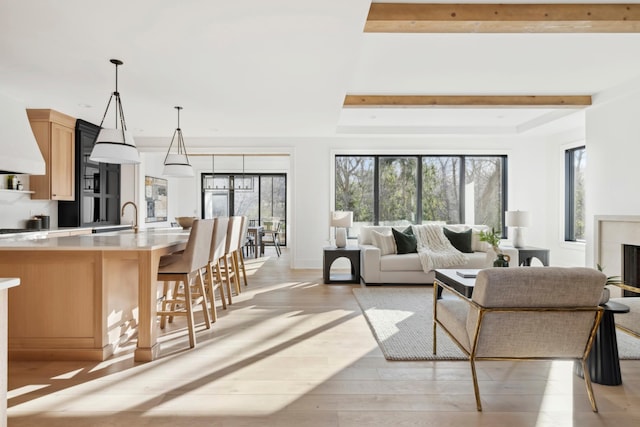 living room featuring beamed ceiling, light hardwood / wood-style floors, and sink