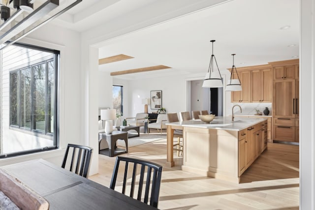 kitchen featuring light brown cabinetry, sink, pendant lighting, a center island with sink, and light hardwood / wood-style floors