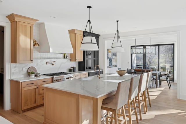 kitchen with sink, stainless steel gas cooktop, light hardwood / wood-style flooring, a kitchen island with sink, and custom range hood