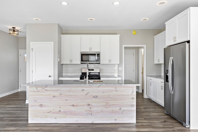 kitchen featuring light stone counters, white cabinetry, stainless steel appliances, and an island with sink