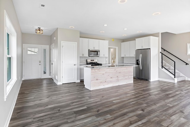 kitchen with white cabinetry, stainless steel appliances, dark hardwood / wood-style flooring, backsplash, and a kitchen island with sink