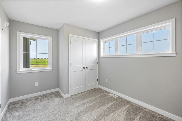 unfurnished bedroom with light carpet, a closet, and multiple windows