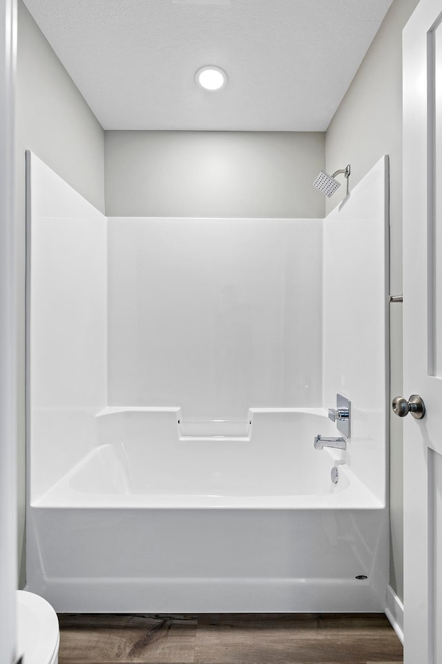 bathroom with hardwood / wood-style flooring,  shower combination, and toilet