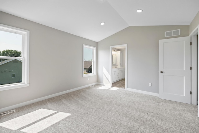 unfurnished bedroom with ensuite bathroom, vaulted ceiling, light colored carpet, and multiple windows