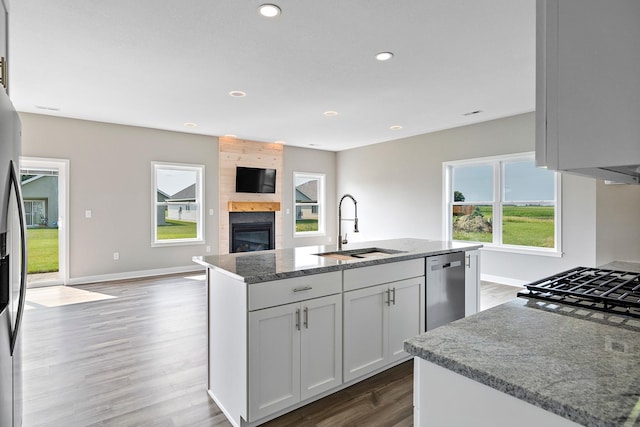 kitchen with dishwasher, white cabinets, sink, light stone countertops, and an island with sink