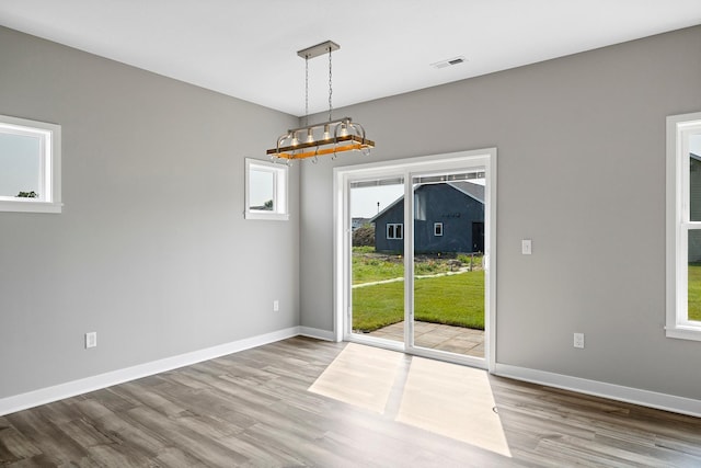 unfurnished dining area with wood-type flooring and an inviting chandelier