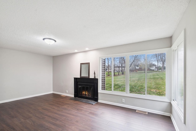 unfurnished living room with a textured ceiling, dark hardwood / wood-style floors, and a wealth of natural light