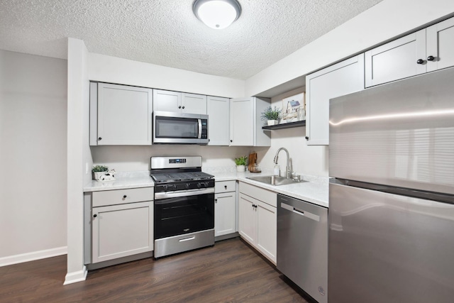 kitchen with a textured ceiling, sink, appliances with stainless steel finishes, and dark wood-type flooring