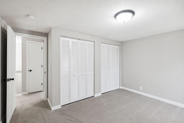 unfurnished bedroom featuring light colored carpet, a textured ceiling, and multiple closets