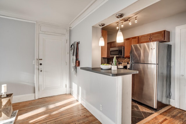 kitchen with pendant lighting, crown molding, hardwood / wood-style flooring, appliances with stainless steel finishes, and kitchen peninsula