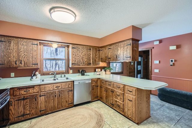 kitchen with a wainscoted wall, light countertops, stainless steel dishwasher, a sink, and a peninsula