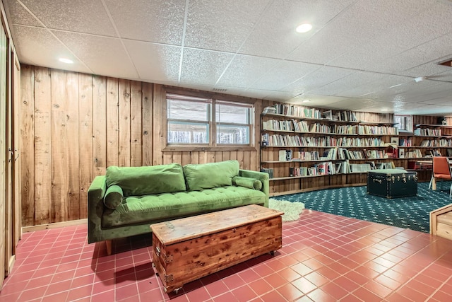 living area with a paneled ceiling, wood walls, and tile patterned floors