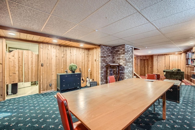 interior space with a paneled ceiling, wood walls, and carpet flooring