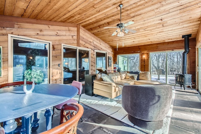 sunroom featuring lofted ceiling, a wood stove, wooden ceiling, and ceiling fan