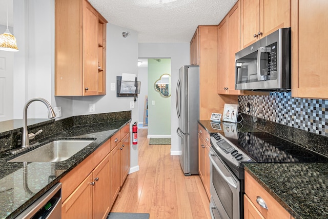 kitchen with appliances with stainless steel finishes, sink, dark stone countertops, and light hardwood / wood-style flooring