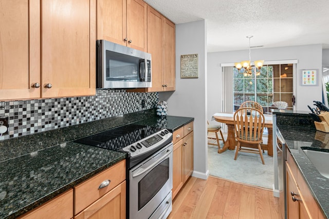 kitchen with an inviting chandelier, light hardwood / wood-style flooring, hanging light fixtures, appliances with stainless steel finishes, and dark stone counters