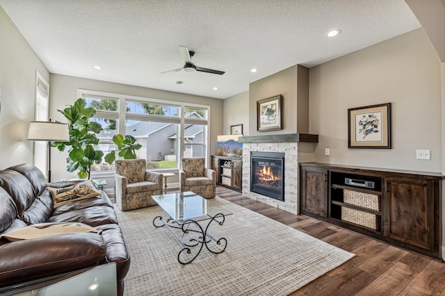 living room featuring hardwood / wood-style flooring, a fireplace, ceiling fan, and a textured ceiling