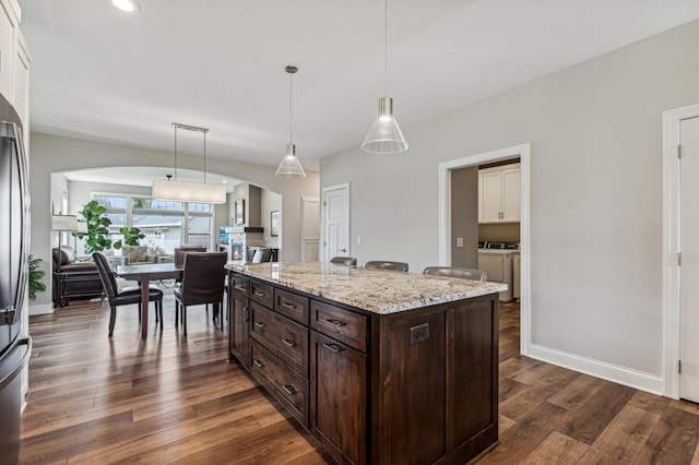 kitchen featuring dark brown cabinets, a center island, hanging light fixtures, and dark wood-type flooring