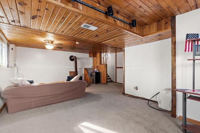 basement with carpet flooring, wooden ceiling, ceiling fan, and a wood stove