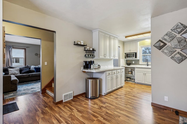 kitchen with white cabinets, a wealth of natural light, light hardwood / wood-style flooring, and stainless steel microwave