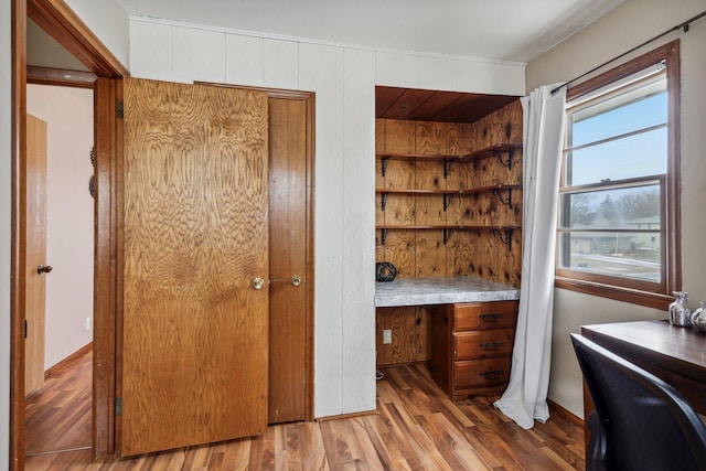 unfurnished office with light wood-type flooring, built in desk, and wooden walls