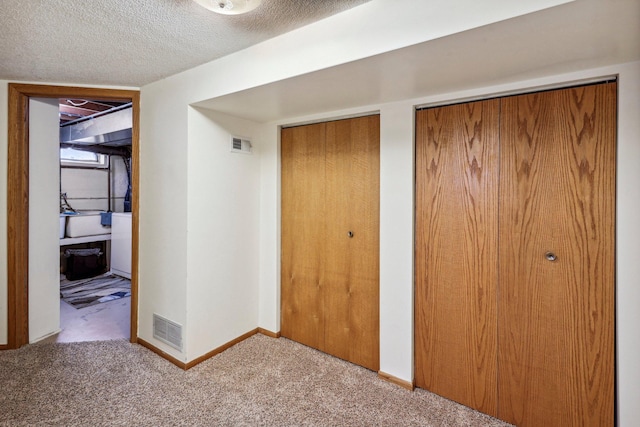 unfurnished bedroom featuring carpet flooring, a textured ceiling, and two closets