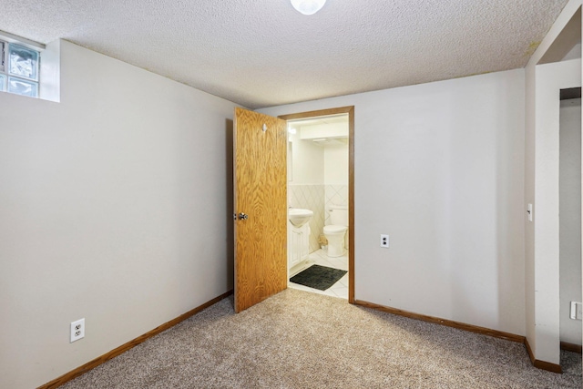 unfurnished bedroom with ensuite bath, carpet floors, and a textured ceiling