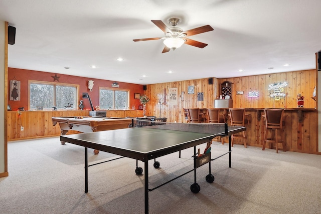 playroom with ceiling fan, light colored carpet, wooden walls, and bar