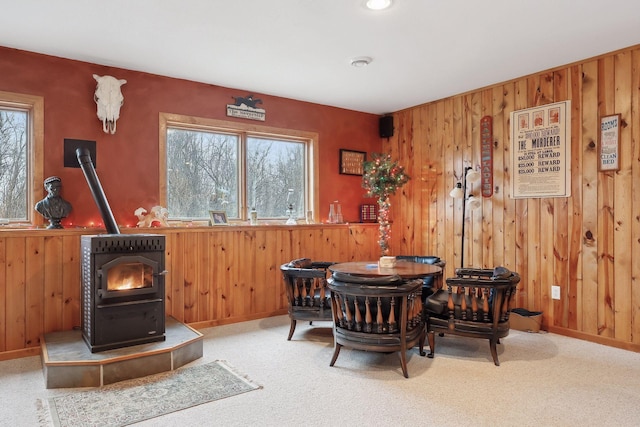 sitting room featuring wooden walls, a wood stove, and carpet flooring