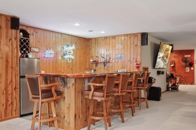 bar featuring wooden walls, light carpet, and stainless steel refrigerator