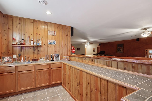 bar with tile counters, ceiling fan, wooden walls, sink, and light tile patterned flooring