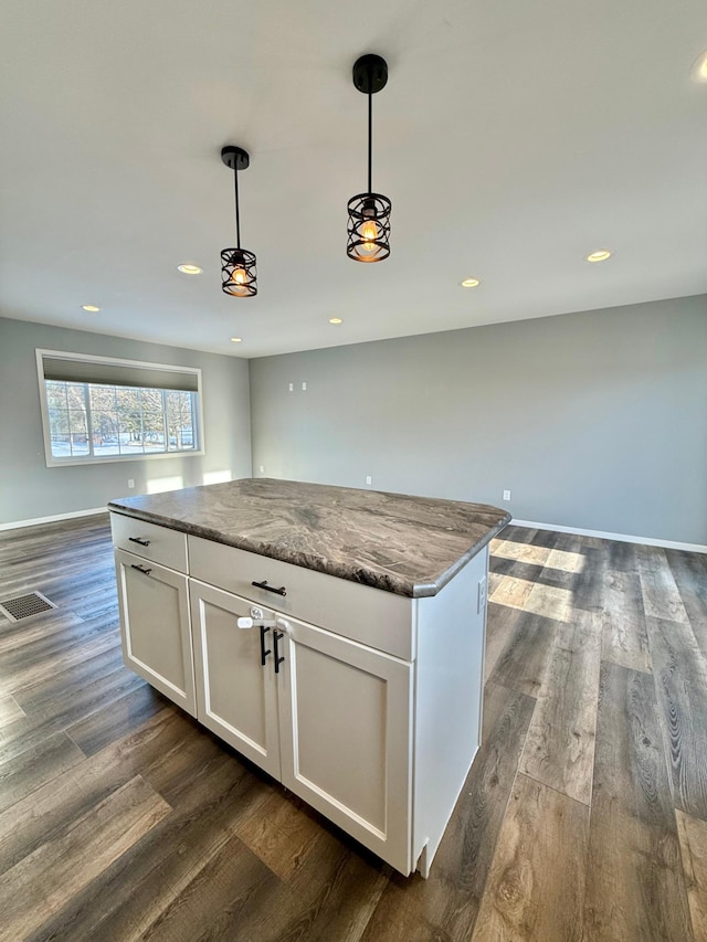 kitchen featuring white cabinetry, light stone counters, pendant lighting, and dark hardwood / wood-style floors