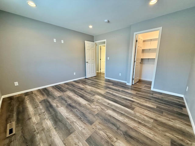 unfurnished bedroom with a spacious closet, dark wood-type flooring, and a closet