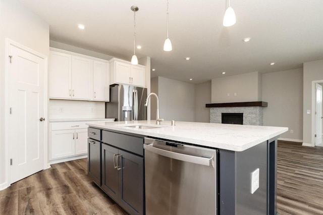 kitchen featuring appliances with stainless steel finishes, pendant lighting, white cabinetry, light stone counters, and a center island with sink