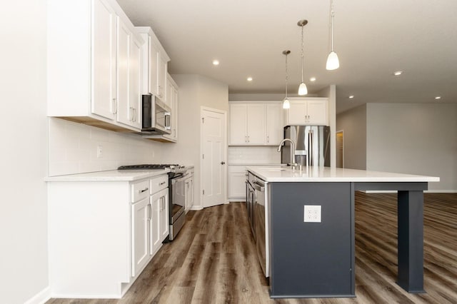 kitchen featuring pendant lighting, stainless steel appliances, white cabinets, and a center island with sink