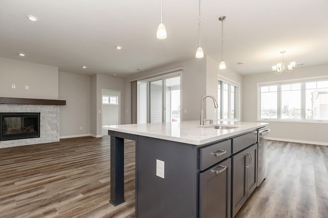 kitchen with hanging light fixtures, sink, a kitchen island with sink, and light stone counters