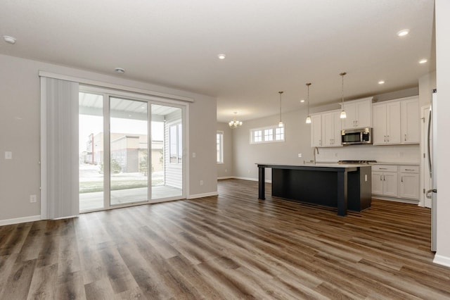 kitchen with decorative light fixtures, an island with sink, white cabinets, dark wood-type flooring, and an inviting chandelier