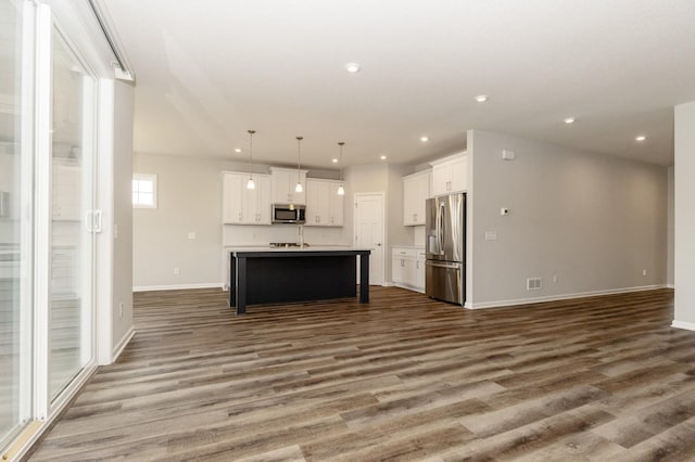 kitchen with a kitchen island with sink, decorative light fixtures, stainless steel appliances, and white cabinets