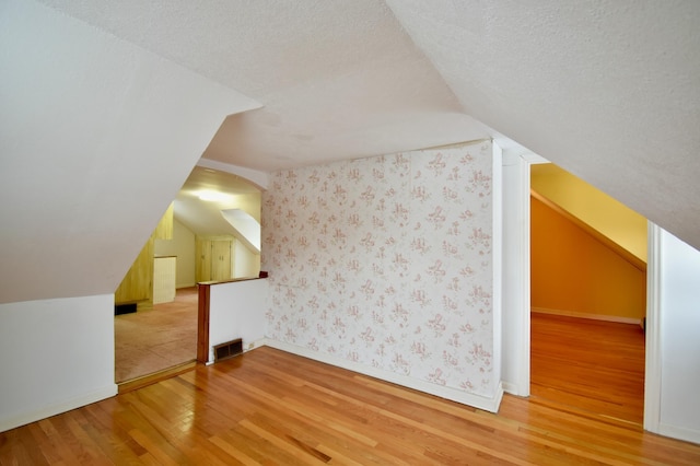 additional living space featuring lofted ceiling, wood-type flooring, and a textured ceiling