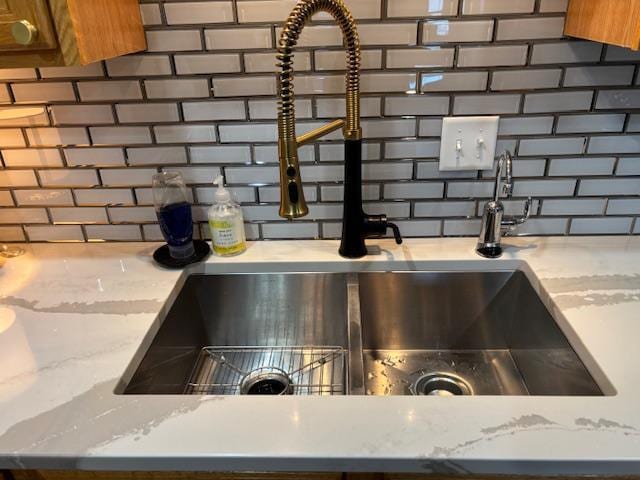 interior details featuring light stone countertops, decorative backsplash, and sink