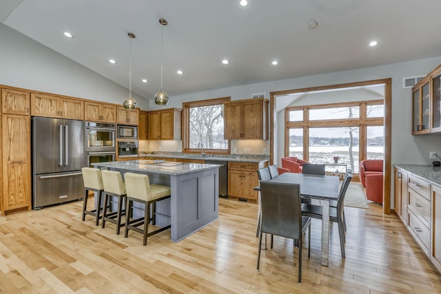 5517 Dickson Rd, Minnetonka, MN 55345 - kitchen with stainless steel appliances, lofted ceiling, a kitchen breakfast bar, a kitchen island, and light stone counters