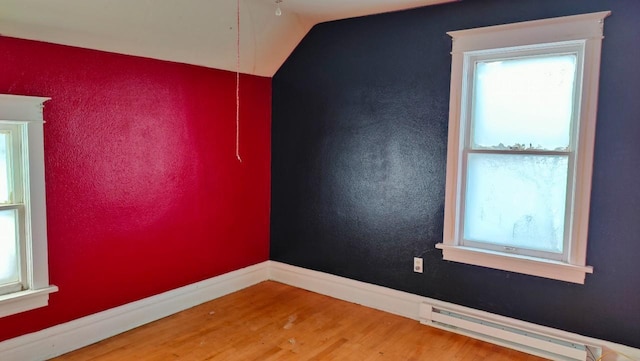 spare room with wood-type flooring, vaulted ceiling, and a baseboard heating unit