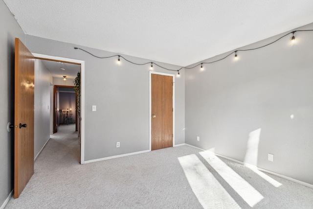 empty room with light colored carpet, a textured ceiling, and baseboards