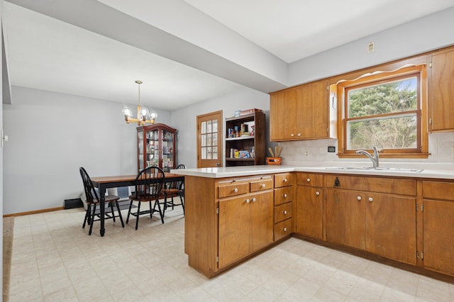 kitchen featuring a peninsula, a sink, brown cabinets, light floors, and light countertops