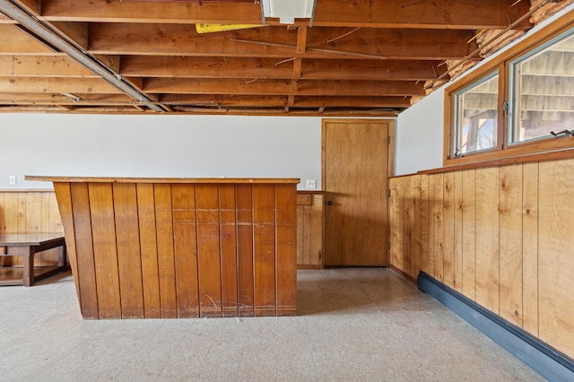 below grade area featuring a baseboard heating unit, a wainscoted wall, wood walls, and light floors