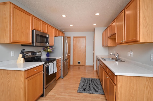 kitchen featuring sink, light hardwood / wood-style floors, a textured ceiling, and appliances with stainless steel finishes