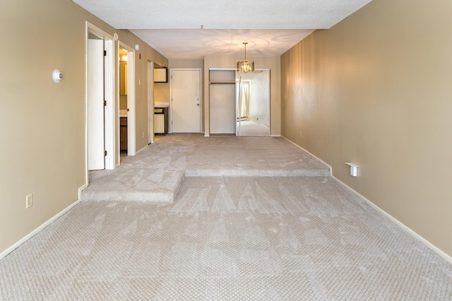 corridor featuring a textured ceiling, light carpet, and an inviting chandelier