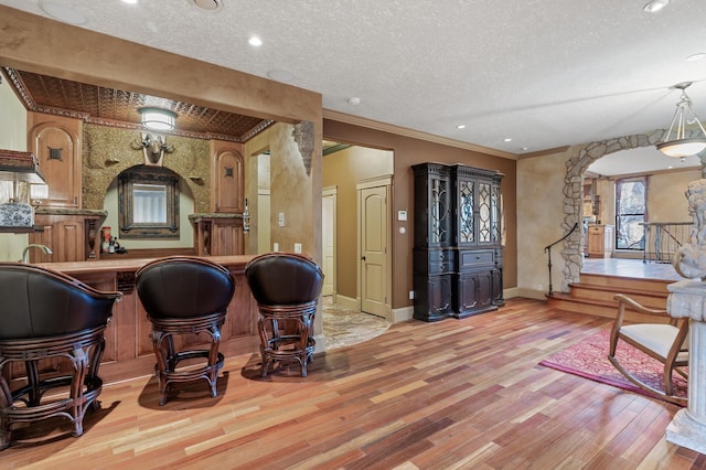 bar with light hardwood / wood-style floors, ornamental molding, and a textured ceiling