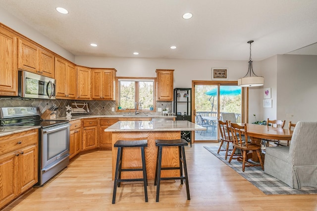 kitchen featuring appliances with stainless steel finishes, light hardwood / wood-style floors, a kitchen island, and hanging light fixtures