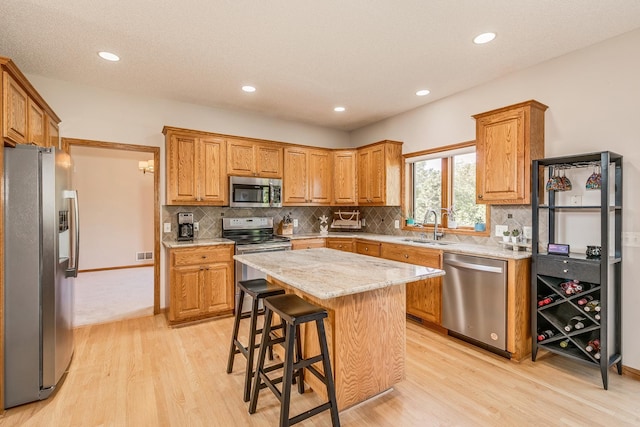 kitchen with a center island, sink, stainless steel appliances, light hardwood / wood-style floors, and a kitchen bar